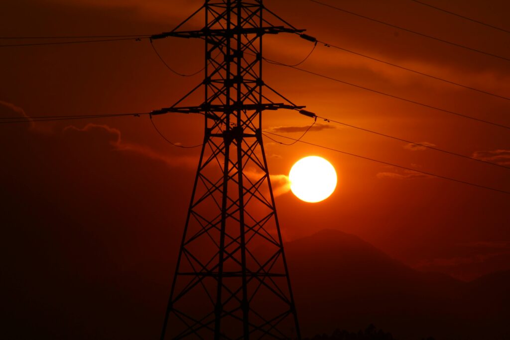 Stunning silhouette of an electric tower against an intense sunset sky with visible power lines.