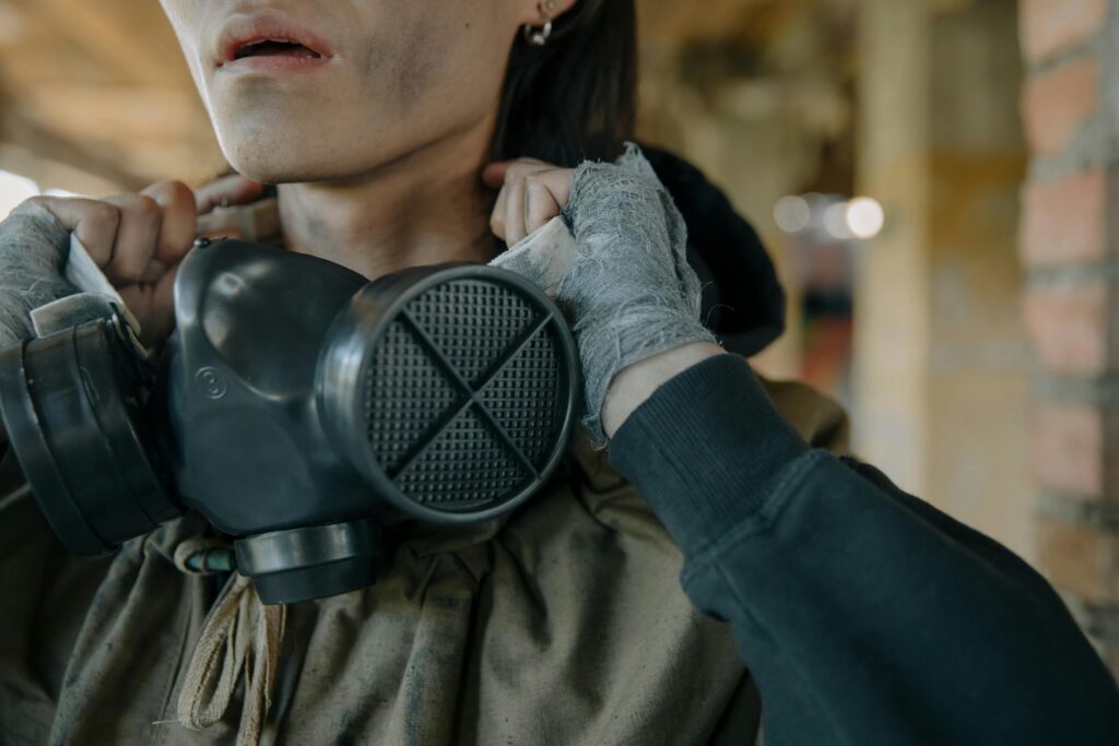 A person with a gas mask and bandaged hands in an urban setting, indicating survival theme.